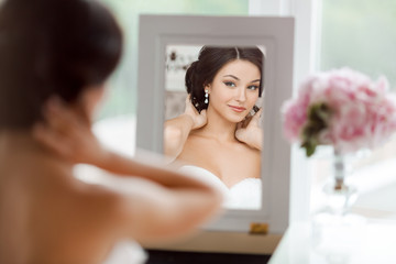 Wall Mural - Portrait of the young beautiful bride looks at herself in the mirror