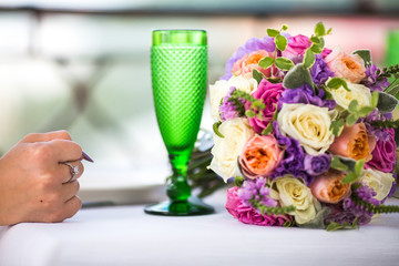 Bride's fist lies before green champagne flute on table with col