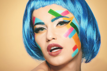 Wall Mural - Face of young woman with creative make up and blue hair on light background