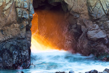 Waves Crash Through The Opening In The Keyhole Arch As Sunset Light Illuminates The Spray With Deep Orange Light