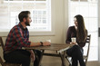© Mint Images - A young man and woman sitting  at a table holding paper cups.