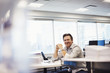 © Mint Images - A man sitting at a table in an office, looking into shot and smiling.