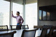 © Mint Images - A man in a meeting room looking out of a window at an urban landscape.