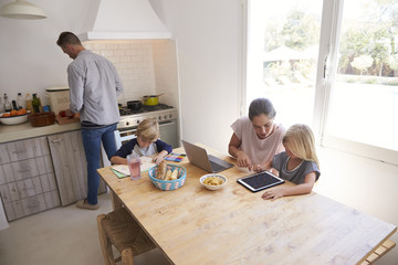 Dad cooking and mum with kids at kitchen table, high angle