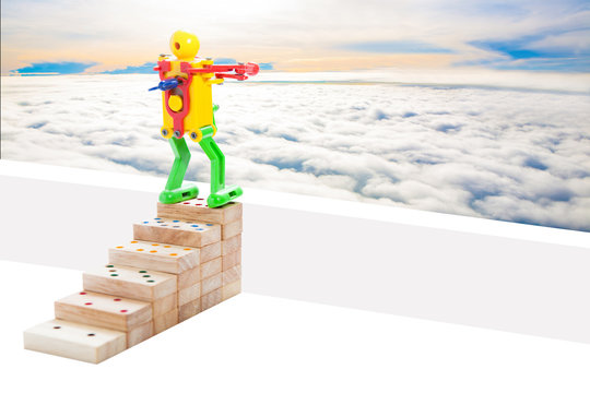 robot toy standing on top steps of wooden domino, on sky backgr