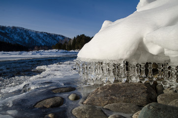 Wall Mural - icicles pose in the spring sun, the river teket in the background, the mountains on the horizon.