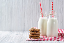 Bottles of milk with red striped straws and chocolate chip cookies on wooden background