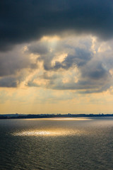 Wall Mural - Beautiful sunrise over the sea in the morning on cloudy day that sun beams break through the clouds. Sun beaming through clouds with urban landscape, if you zoom in will see the small fishing boats.