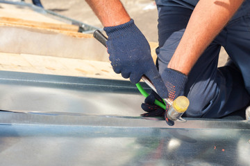 Wall Mural - Roofer builder worker finishing folding a metal sheet using rubber mallet