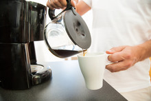 Man In The Kitchen Pouring A Mug Of Hot Filtered Coffee From A Glass Pot. Having Breakfast In The Morning