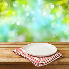 Wall Mural - Empty white plate on wooden table over blurred bokeh nature background