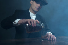 Retro 1920s English Gangster With Flat Cap Pouring Whiskey. Peak