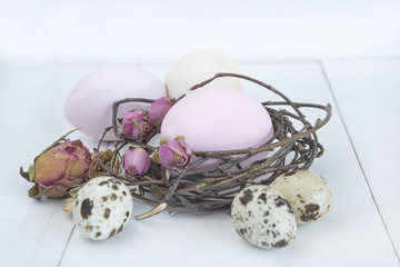 easter concept/hand peinted eggs and quail eggs in a nest with rose flowers on white wooden background