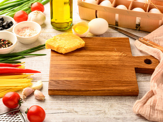 Ingredients for cooking healthy Italian food and cutting board on a white wooden table with space for an object in a home 