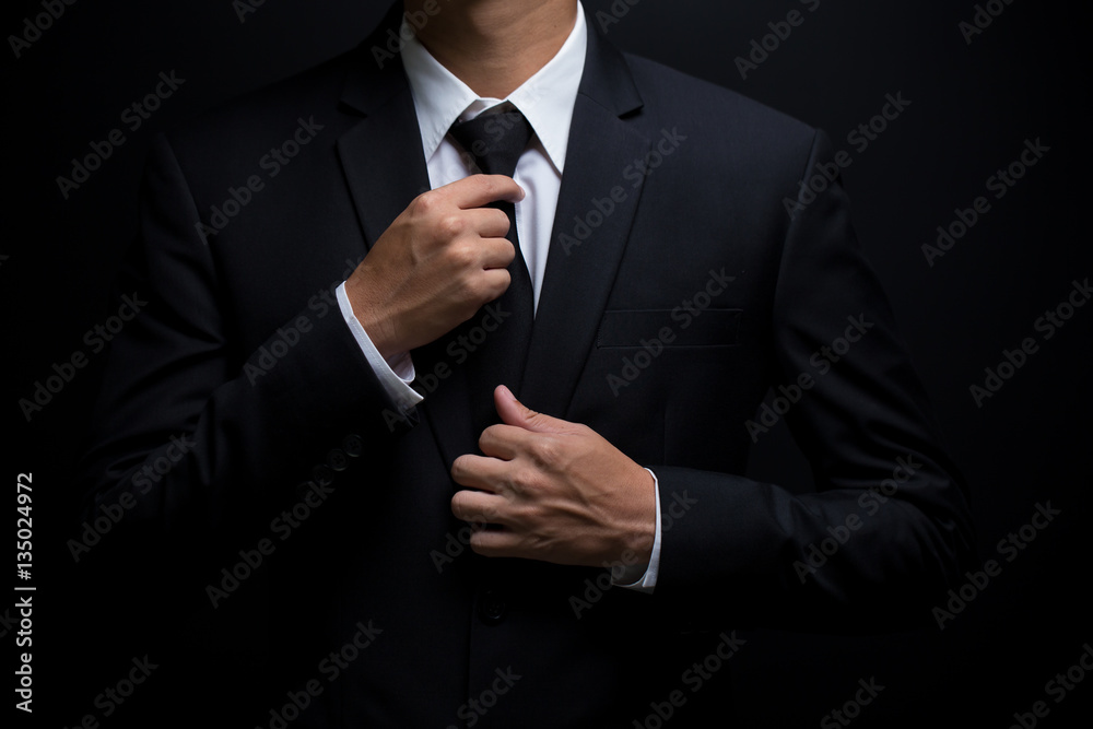 Man in black suit and adjusting his necktie - obrazy, fototapety, plakaty 