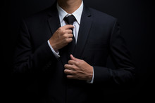Man In Black Suit And Adjusting His Necktie