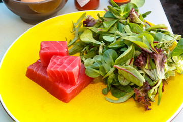 Wall Mural - Slices of raw tuna with greens are on the plate.