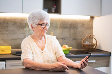 Elderly woman sitting at table and using a smartphone.