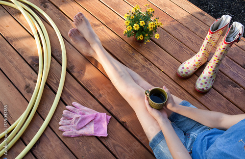 Fotografie, Obraz Woman with cup of coffee sitting on a patio wooden deck resting after working in