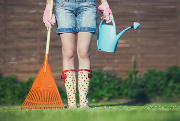 Woman wearing gloves and wellington boots holding rake and water can, spring gardening concept