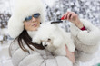 © Addoro - Winter time fun. Woman wearing fur hat and winter coat holding her dog while she is grooming him. Brushing the dog in the winter time.
