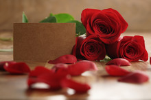 Three Red Roses And Petals On Old Wood Table With Paper Card, Romantic Background