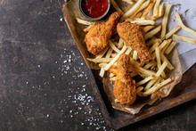 Fast Food Fried Crispy Chicken Legs And French Fries Potatoes With Salt And Ketchup Sauce Served On Baking Paper In Old Rusty Oven Tray Over Dark Texture Background. Top View, Space For Text