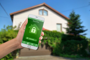 Wall Mural - Smartphone with home security app in a hand on the building background