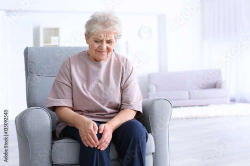 Fotografiet Elderly woman suffering from pain in knee at home