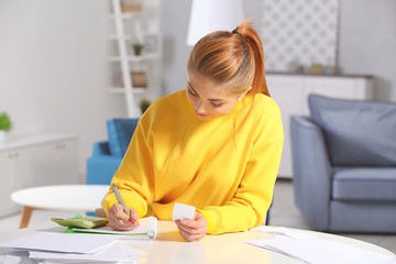 Beautiful young woman calculating taxes at home