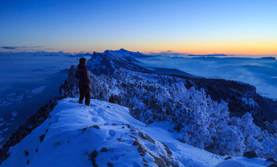 Fototapete - Hiker looking over a snow covered mountain range, Vercors, France, during a winter sunset.