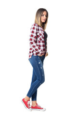 Wall Mural - Side view of serious young beautiful girl with hands in pockets walking and looking down. Full body length portrait isolated over white studio background.