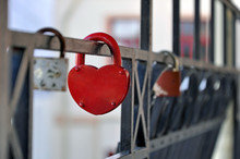Black Metal Fence With Hanging Red Closed Padlock In The Shape Of Heart Close Up.