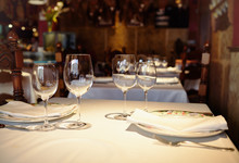 Empty Glasses In A Restaurant On White Tablecloth. Shade, Brown Background And Carved Chairs.
