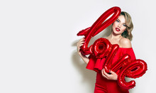 Valentine's Day. Word Love Letters From The Inflatable. Girl Holding A Big Word Love.Girl With Retro Hairstyle In Red Dress In Red High Heels In Studio On A White Background.