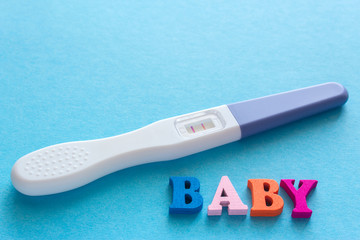 baby word from wooden letters, positive pregnancy test with two stripes on a blue background