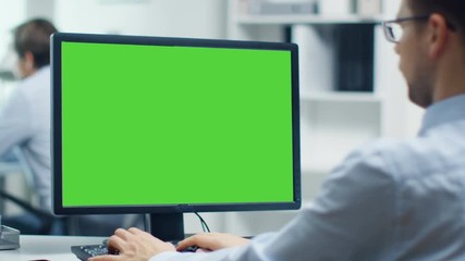Businessman Working on a Personal Computer with Green Screen on. Colleague in the Background. Office is Bright and Modern. Shot on RED Cinema Camera 4K (UHD).