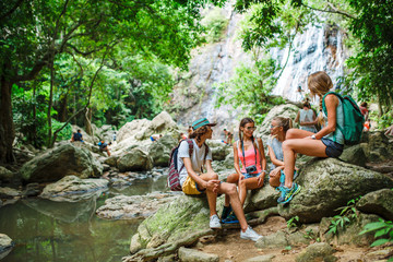 tourists sitting on rocks talking in front of jungle river with waterfall