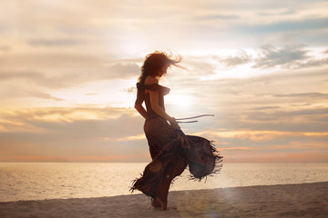 beautiful young woman walking on the beach. woman silhouette at sunset