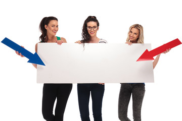 Wall Mural - happy casual women pointing arrows to a big blank board