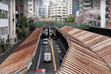 A Scene Of A Busy Japanese Road At The Day Time Can Be Seen In The Picture And At The Background We Can Also See A Foot Bridge.