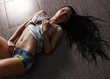 © iproname - Girl with long dark hair in blue jeans shorts lying on the floor. She shows her sexy body and belly