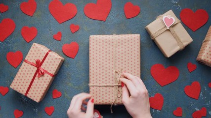 Wall Mural - Woman's hands unwrapping Valentine's Day holiday gift box concept of romantic love. Slider dolly move, overhead shot. Vintage blue table with red hearts decorations flat lay. Blank space for design