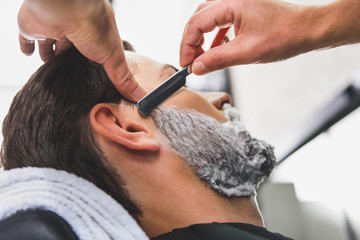 Wall Mural - Skillful hairdresser shaving beard by blade