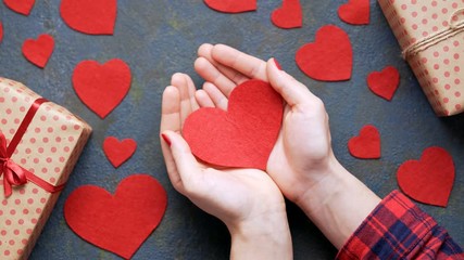 Wall Mural - Woman's hands appers in frame with red heart Valentine's Day symbol concept of gentle love gift on vintage blue table background. Flat lay top view