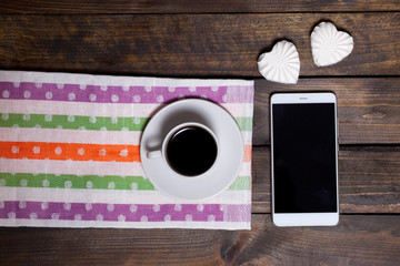 White mug of coffee and two marshmallows in the shape of hearts on a wooden background for breakfast