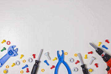 Colorful kids toys plastic bolts, nuts, screwdrivers, pliers, drill and other construction tools frame on white background. Top view. Flat lay. Copy space for text