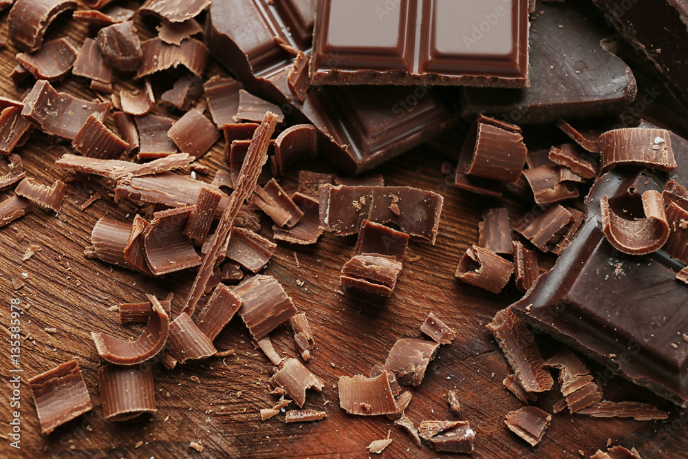 Broken chocolate pieces and shavings on wooden background