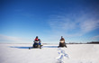 A man and hid teenage daughter wearing helmets and winter gear parked side by side on their snowmobiles in a white winter landscape