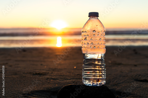 Fotografia, Obraz Plastic bottle of water on the beach at sunset , sunrise time